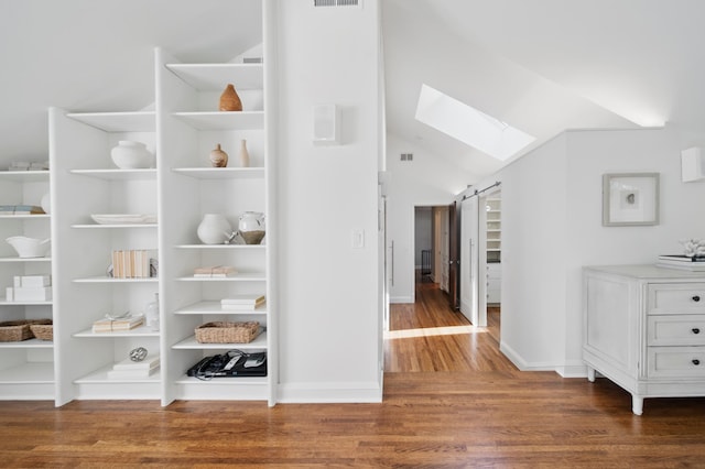 hallway with a skylight, wood finished floors, baseboards, and lofted ceiling