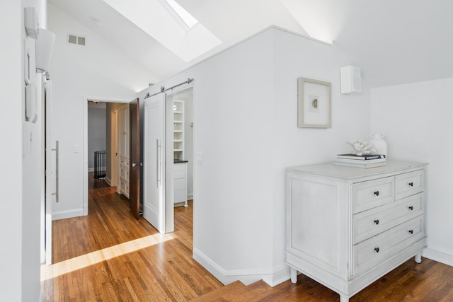hall featuring vaulted ceiling, a skylight, wood finished floors, baseboards, and a barn door