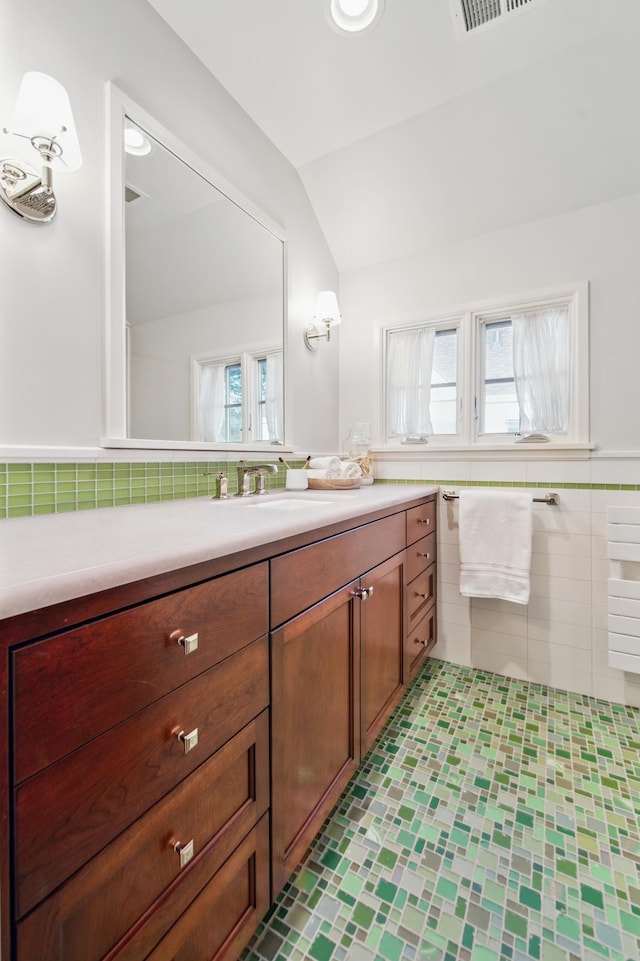 bathroom with vaulted ceiling, vanity, tile walls, tile patterned flooring, and wainscoting