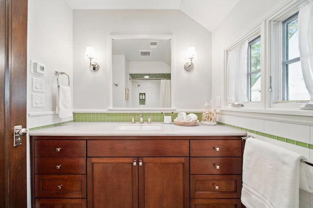 full bathroom with vaulted ceiling, vanity, curtained shower, wainscoting, and tile walls
