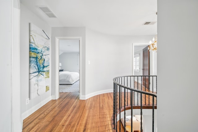 corridor with an upstairs landing, light wood finished floors, a chandelier, and baseboards
