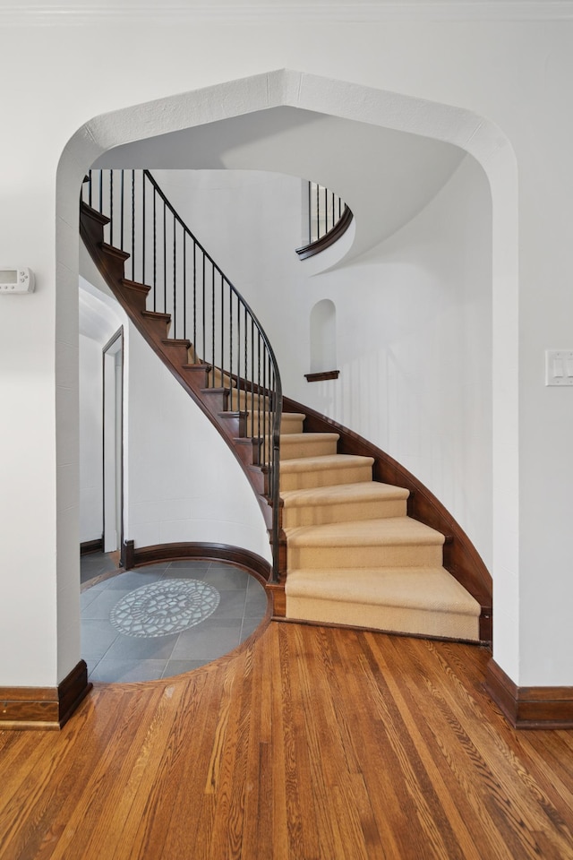 staircase featuring baseboards, arched walkways, and wood finished floors