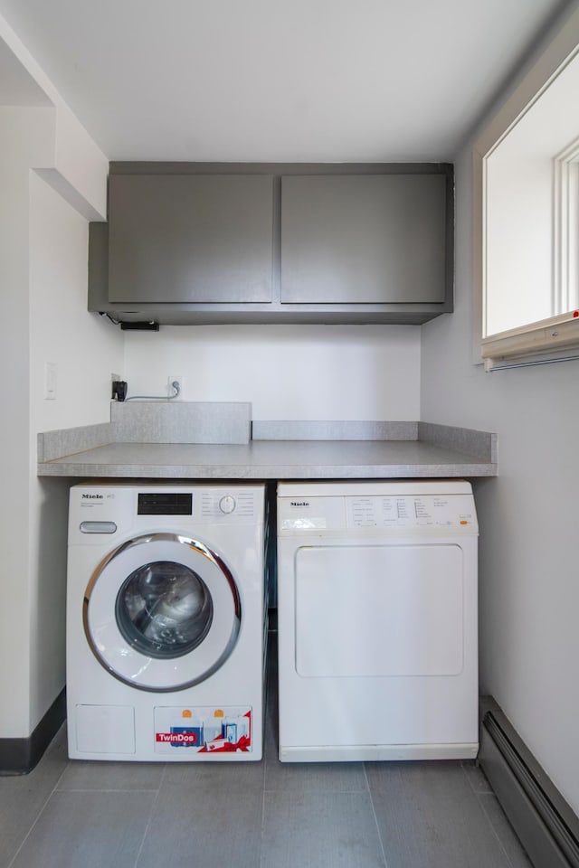 clothes washing area featuring washer and dryer, dark tile patterned flooring, a baseboard radiator, cabinet space, and baseboards
