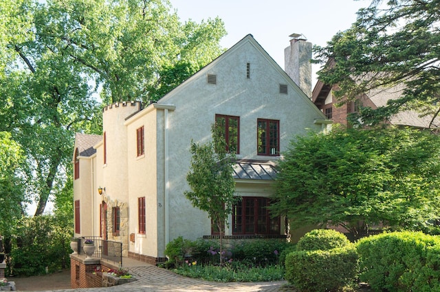 view of front facade with stucco siding, a standing seam roof, a chimney, and metal roof