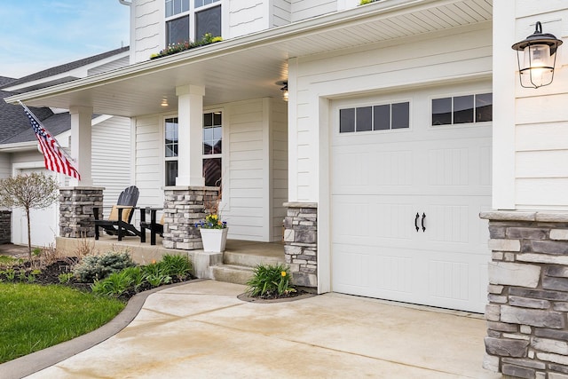 view of exterior entry featuring a porch, driveway, stone siding, and a garage