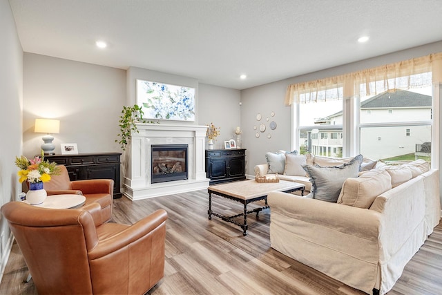living area with recessed lighting, a glass covered fireplace, and wood finished floors