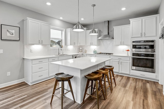 kitchen with a kitchen breakfast bar, wall chimney range hood, white cabinets, a sink, and appliances with stainless steel finishes