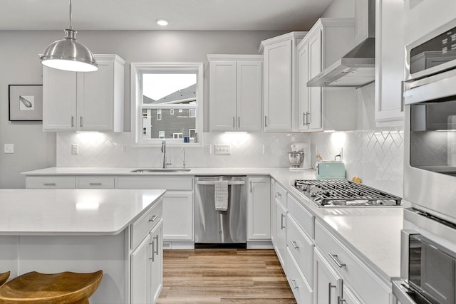 kitchen with white cabinets, appliances with stainless steel finishes, a sink, light countertops, and wall chimney exhaust hood