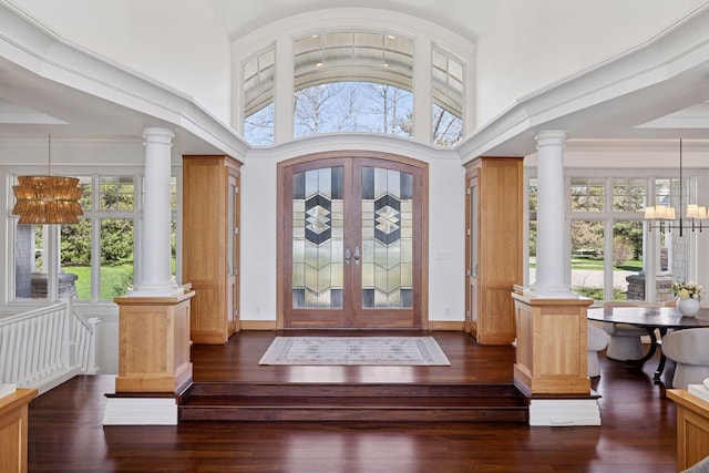 foyer entrance featuring decorative columns, french doors, dark wood finished floors, high vaulted ceiling, and a notable chandelier