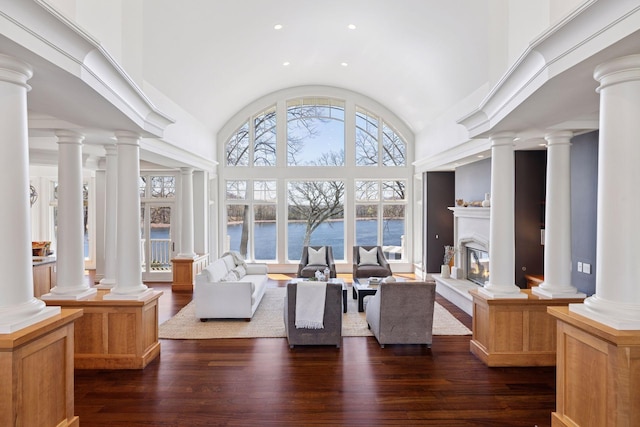 interior space featuring high vaulted ceiling, a glass covered fireplace, recessed lighting, a water view, and dark wood-style floors