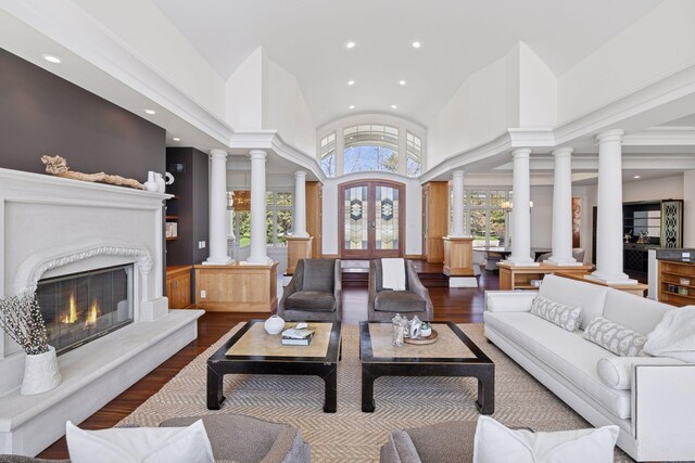 living room featuring a fireplace, high vaulted ceiling, recessed lighting, wood finished floors, and ornate columns
