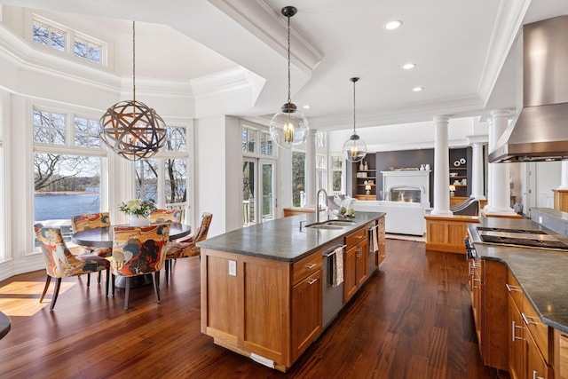 kitchen with wall chimney range hood, appliances with stainless steel finishes, brown cabinets, a sink, and a chandelier