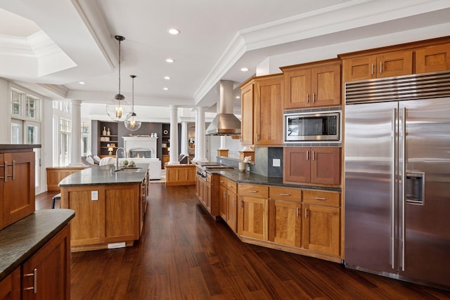 kitchen with island exhaust hood, a sink, open floor plan, built in appliances, and ornate columns