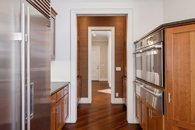 kitchen featuring baseboards, dark wood-style floors, a warming drawer, ornamental molding, and stainless steel appliances