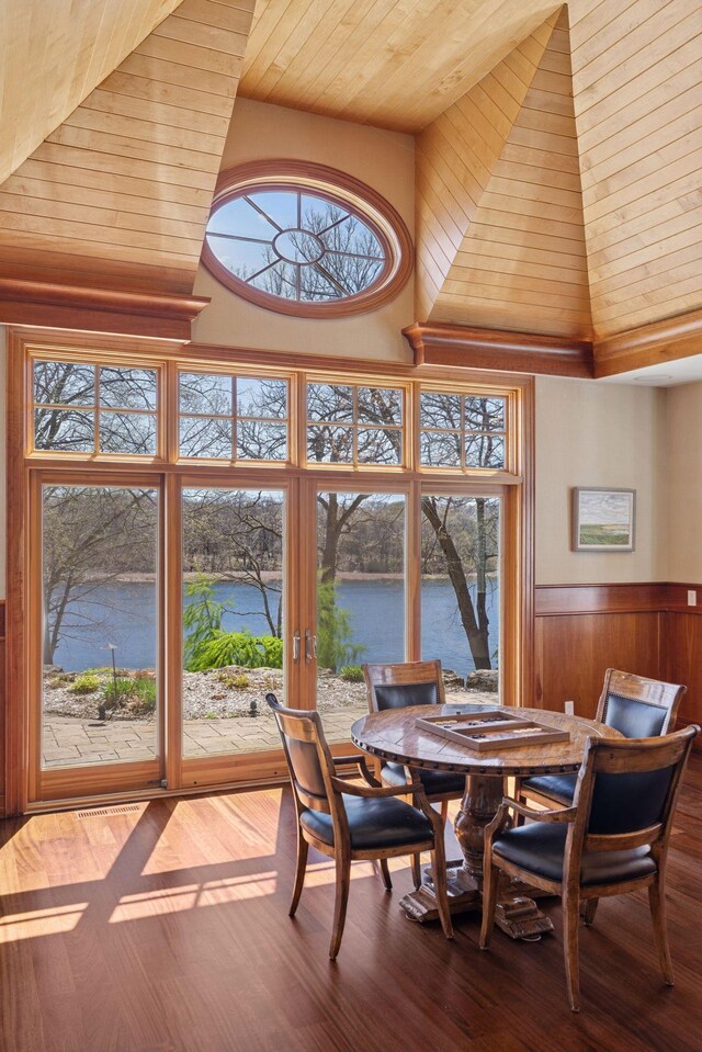 dining room with wood ceiling, wood finished floors, high vaulted ceiling, wooden walls, and a water view