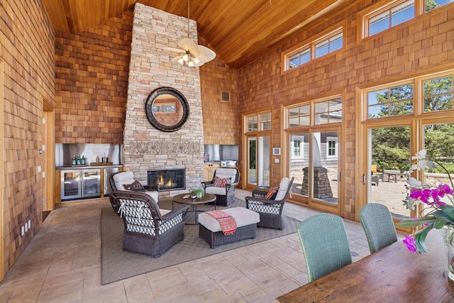living area with plenty of natural light, wood ceiling, an outdoor stone fireplace, and high vaulted ceiling