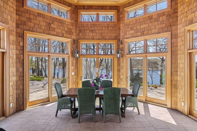 sunroom featuring a water view, stone tile floors, plenty of natural light, and a towering ceiling