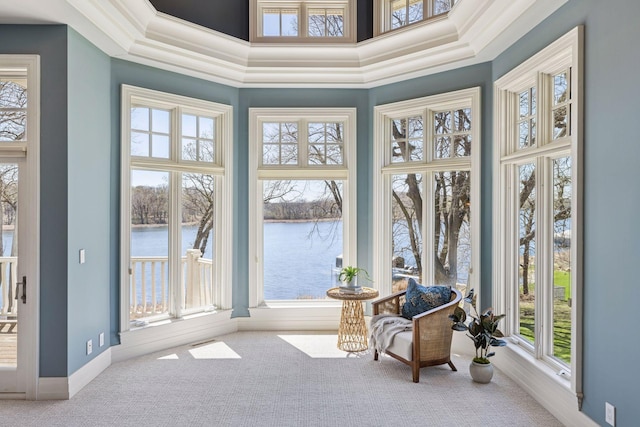 sunroom / solarium with carpet flooring, a towering ceiling, and a water view