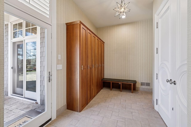 mudroom with stone tile floors, wallpapered walls, visible vents, and an inviting chandelier