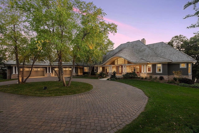view of front of home featuring a lawn, curved driveway, a chimney, and a garage