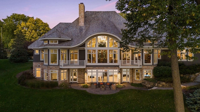 rear view of property with a chimney, a yard, a patio area, and stone siding