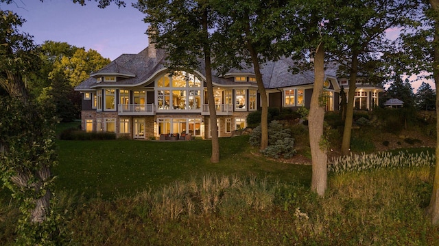 back of property at dusk featuring brick siding and a lawn
