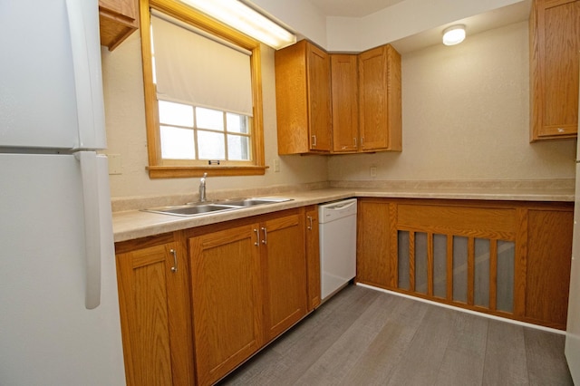 kitchen featuring brown cabinetry, light countertops, a sink, and white appliances