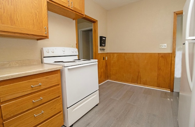 kitchen with white appliances, light wood-style flooring, a wainscoted wall, light countertops, and brown cabinets