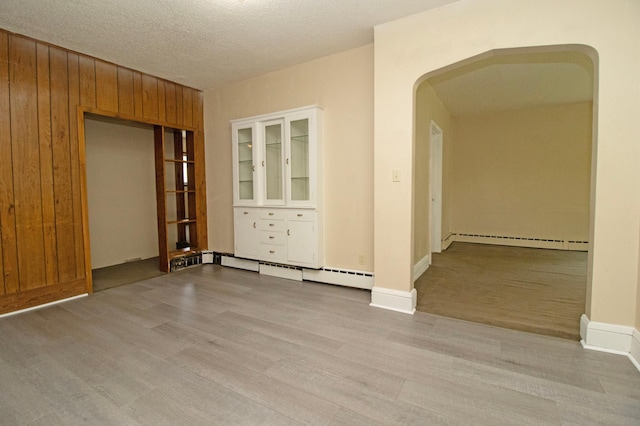 spare room with baseboard heating, arched walkways, wood walls, and light wood-style flooring