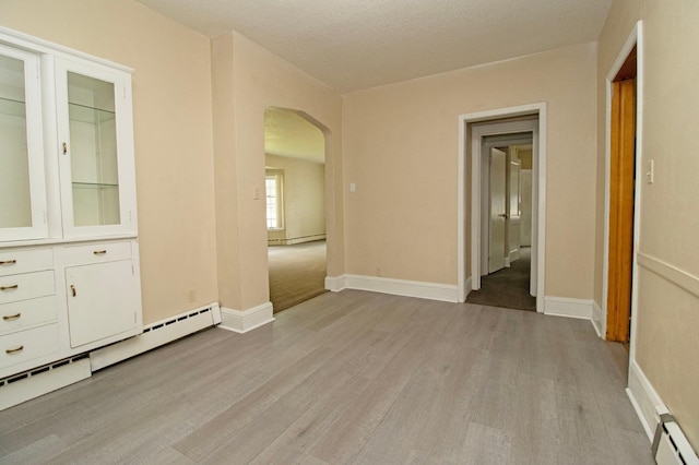 spare room with light wood-style flooring, arched walkways, and a baseboard heating unit