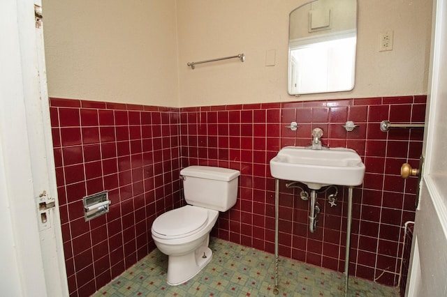 bathroom featuring tile patterned flooring, a wainscoted wall, toilet, tile walls, and a sink