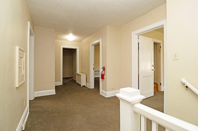 corridor with dark colored carpet, baseboards, an upstairs landing, a textured ceiling, and radiator heating unit