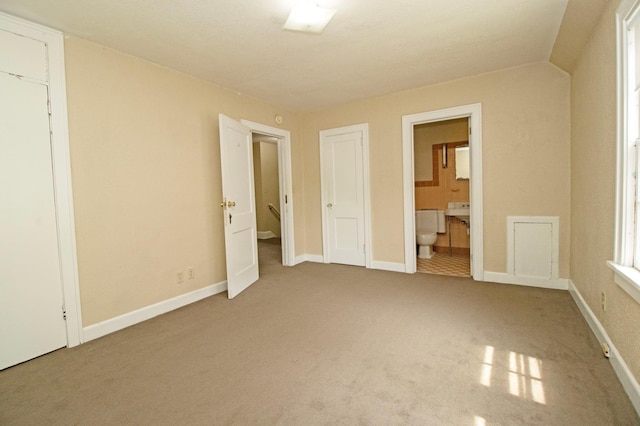 unfurnished bedroom featuring carpet, ensuite bathroom, and baseboards