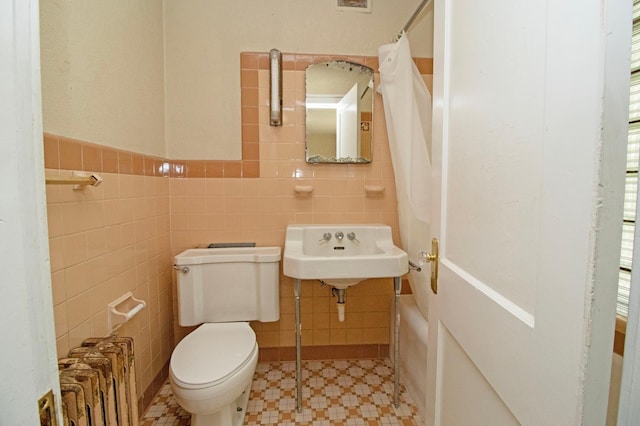 bathroom featuring radiator heating unit, a shower with curtain, toilet, a sink, and tile walls