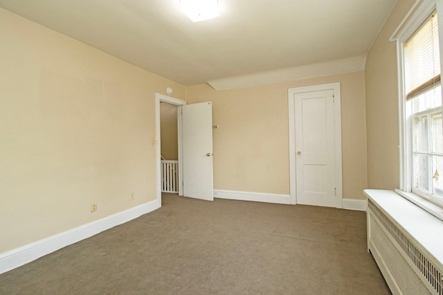 spare room featuring radiator, carpet flooring, and baseboards