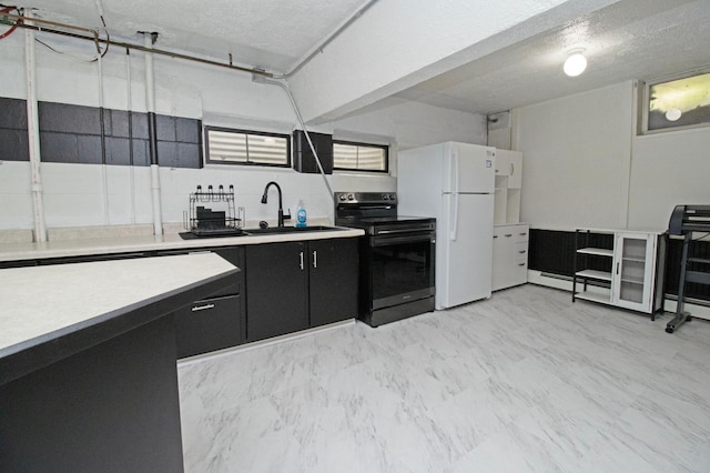 kitchen featuring light countertops, freestanding refrigerator, range with electric cooktop, dark cabinetry, and a sink