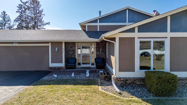 view of front of home with aphalt driveway, a front yard, brick siding, an attached garage, and a shingled roof