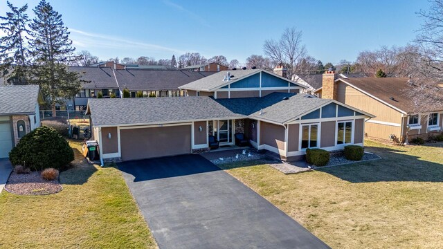 view of front of home featuring roof with shingles, a front yard, an attached garage, driveway, and a residential view
