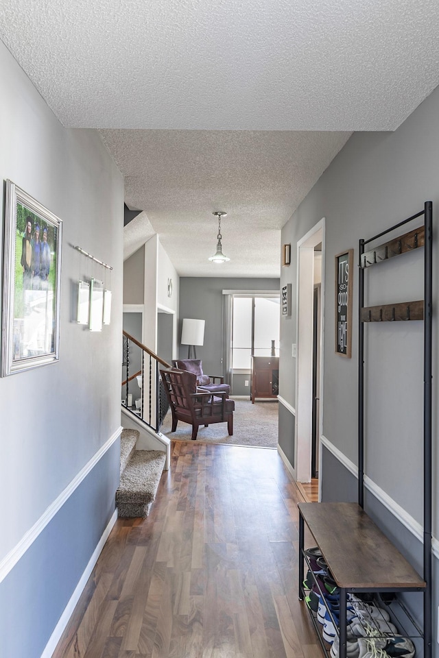 hallway with a textured ceiling, wood finished floors, baseboards, and stairway