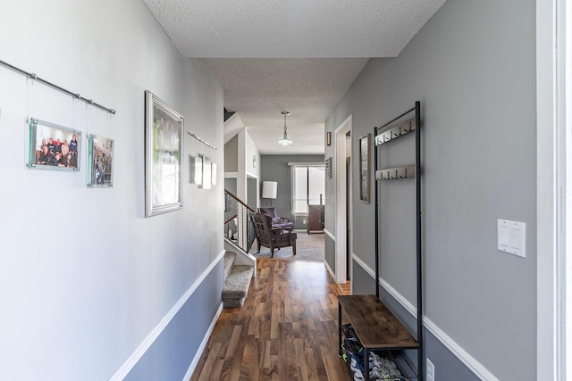 corridor with a textured ceiling, wood finished floors, baseboards, and stairs