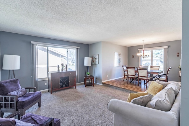 carpeted living area featuring baseboards, a notable chandelier, and a textured ceiling