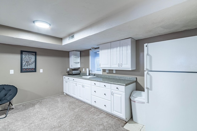 kitchen featuring light carpet, freestanding refrigerator, white cabinets, visible vents, and a sink