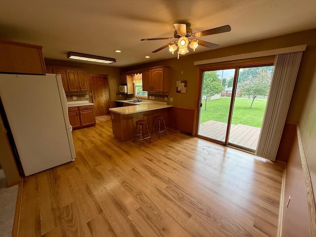 603 Maple Ave, Olivia, MN 56277 - kitchen with white appliances, a peninsula, ceiling fan, light wood-style flooring, and light countertops