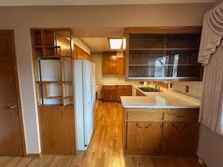 kitchen with light countertops, a sink, open shelves, brown cabinets, and light wood-style flooring