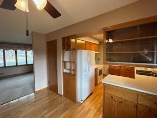 kitchen featuring light countertops, open shelves, white fridge with ice dispenser, light wood-style flooring, and brown cabinetry