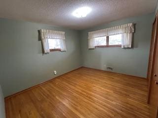 unfurnished bedroom featuring multiple windows, wood finished floors, and a textured ceiling