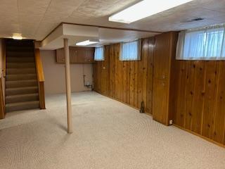 basement with light carpet, wooden walls, and stairs