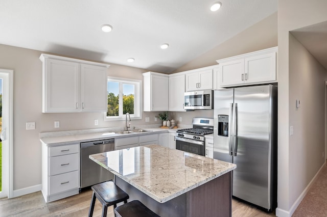 kitchen featuring stainless steel appliances, a kitchen breakfast bar, a sink, vaulted ceiling, and white cabinetry