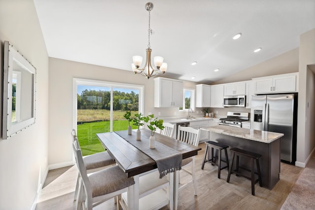 dining area with light wood-type flooring, vaulted ceiling, baseboards, and a chandelier
