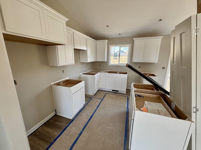 kitchen featuring vaulted ceiling, wood finished floors, washer / dryer, baseboards, and white cabinetry